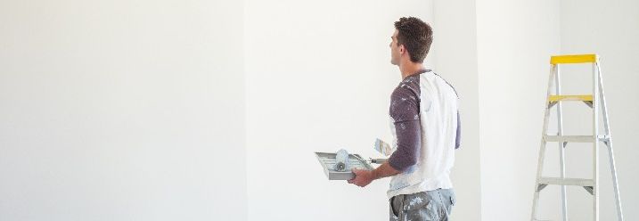 Mann steht vor weißer Wand mit Malerwerkzeug